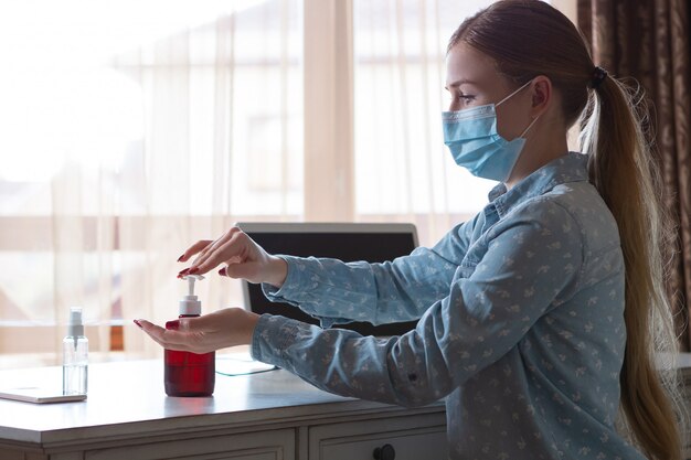 Mujer joven en mascarilla desinfectando superficies de aparatos en su lugar de trabajo