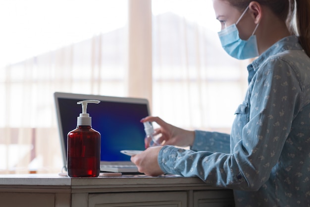 Foto gratuita mujer joven en mascarilla desinfectando superficies de aparatos en su lugar de trabajo