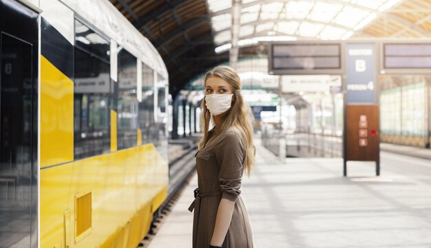 Mujer joven con mascarilla en una estación de tren bajo las luces - covid-19