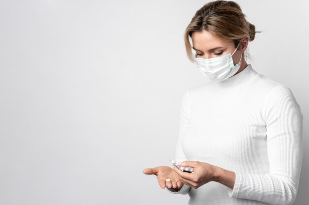 Mujer joven con mascarilla quirúrgica tomando tabletas