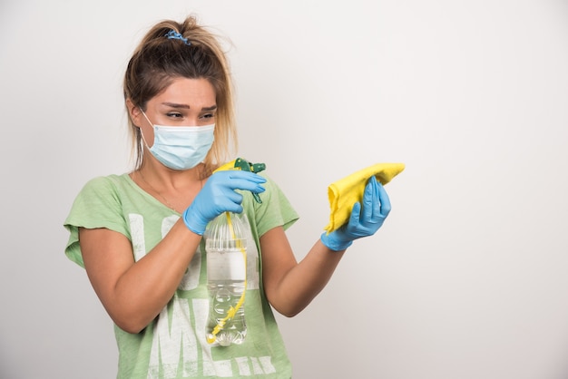 Foto gratuita mujer joven con mascarilla rociando sobre tela en la pared blanca.