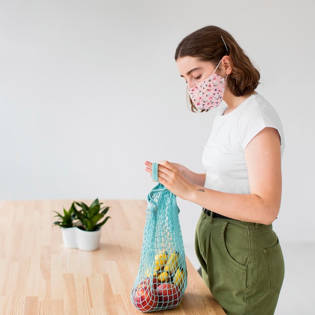 Mujer joven con mascarilla sacando comestibles de la bolsa