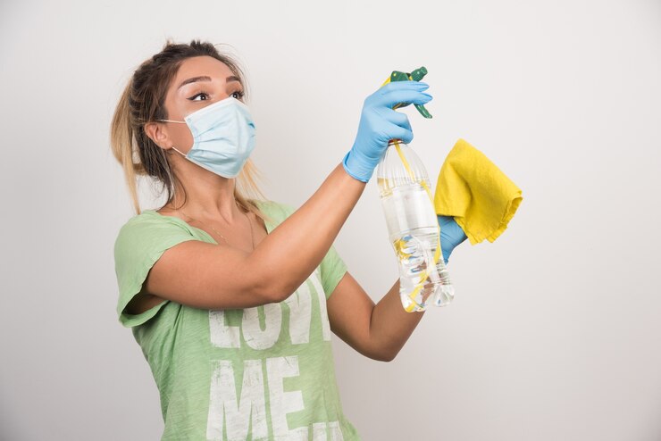 Foto gratuito mujer joven con mascarilla y suministros de pulverización en la pared blanca.