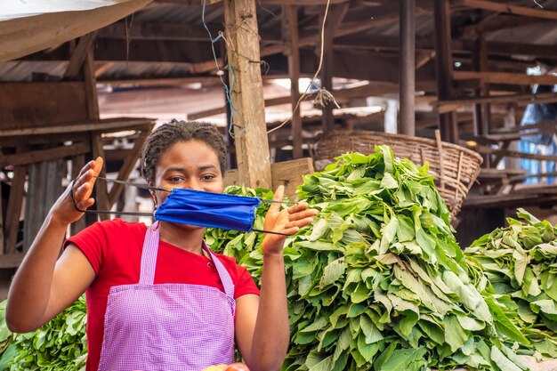 Mujer joven del mercado africano sosteniendo una mascarilla sobre su rostro.