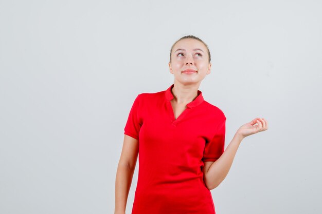 Mujer joven mirando hacia arriba en camiseta roja y mirando esperanzado