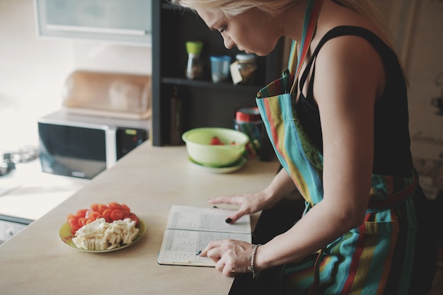 Mujer joven mirando hacia arriba en un libro de recetas