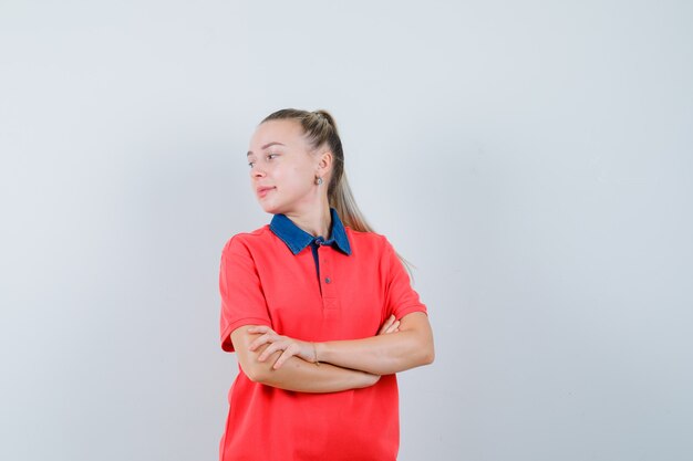 Mujer joven mirando hacia atrás con los brazos cruzados en camiseta y mirando confiado