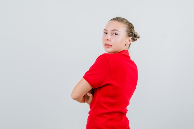 Mujer joven mirando hacia atrás con los brazos cruzados en camiseta roja y mirando confiado. .