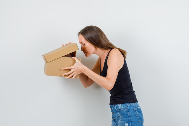 Mujer joven mirando en caja de cartón en camiseta, pantalones cortos.