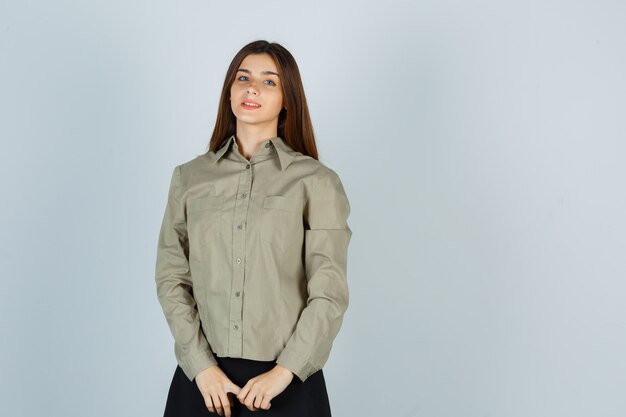 Mujer joven mirando a la cámara en camisa, falda y mirando alegre, vista frontal.