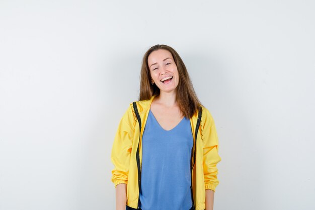 Mujer joven mirando a cámara en camiseta, chaqueta y mirando feliz. vista frontal.