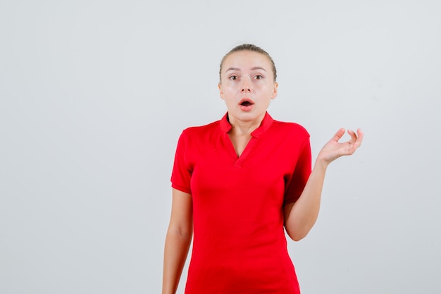 Mujer joven mirando en camiseta roja y mirando perplejo