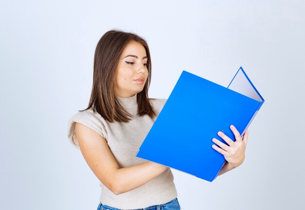 Mujer joven mirando una carpeta azul sobre fondo blanco.