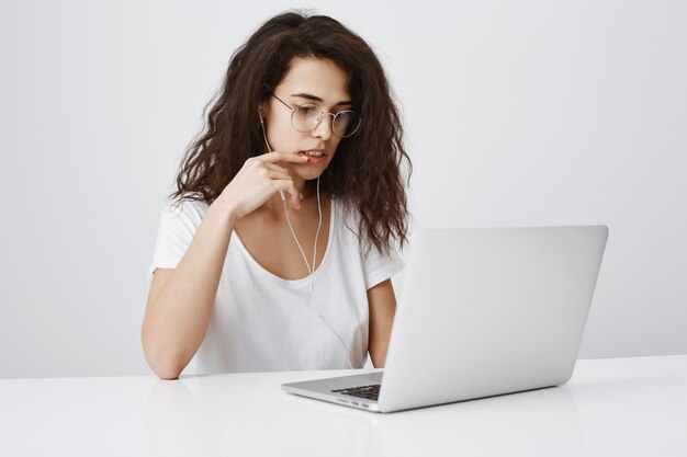 Mujer joven mirando se centró en el proyecto en la computadora portátil, trabajando en la oficina