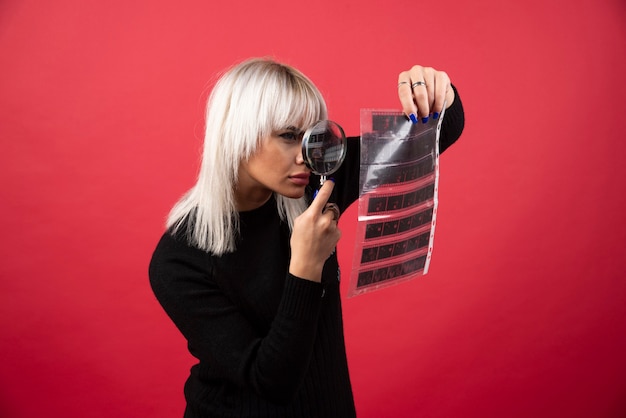 Mujer joven mirando una cinta fotográfica sobre un fondo rojo. Foto de alta calidad