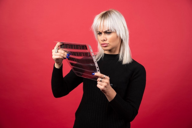 Mujer joven mirando una cinta fotográfica sobre un fondo rojo. Foto de alta calidad