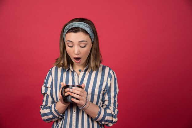 Mujer joven mirando dentro de la taza de café en la pared roja