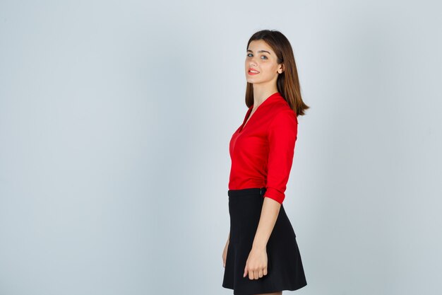 Mujer joven mirando por encima del hombro en blusa roja, falda negra y mirando alegre