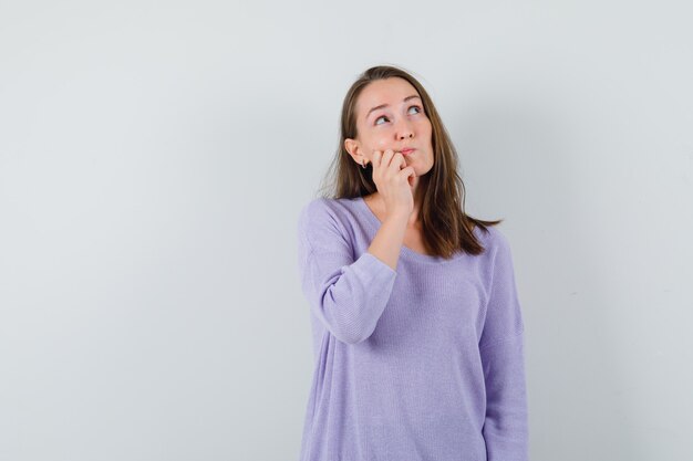 Mujer joven mirando la esquina superior izquierda mientras piensa algo en blusa lila y mira perplejo