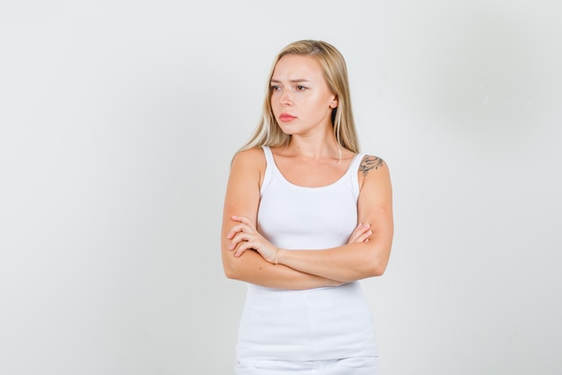Mujer joven mirando a un lado con los brazos cruzados en camiseta, minifalda y mirando triste
