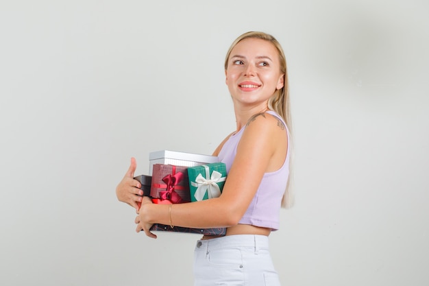 Mujer joven mirando a un lado con cajas de regalo en camiseta, minifalda y mirando alegre.