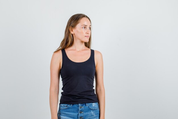 Mujer joven mirando a un lado en camiseta, pantalones cortos y mirando pensativo. vista frontal.