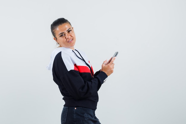 Mujer joven mirando a un lado mientras sostiene el teléfono en la vista frontal de la colorida sudadera.