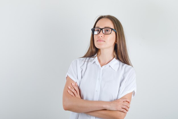 Mujer joven mirando a otro lado con los brazos cruzados en camiseta blanca y gafas