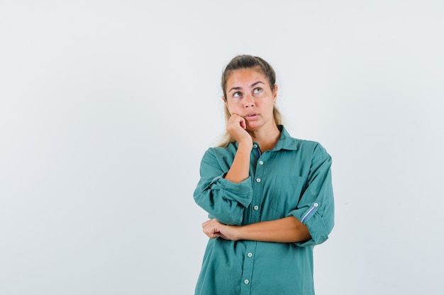 Mujer joven mirando a otro lado mientras se inclina hacia su mano con camisa azul y mirando pensativo