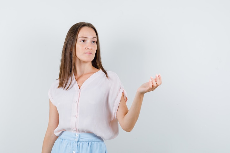 Foto gratuito mujer joven mirando a otro lado con la palma levantada en camiseta, falda y mirando pensativo, vista frontal.
