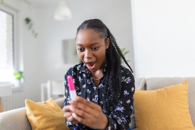 Mujer joven mirando la prueba de embarazo con felicidad Finalmente embarazada Mujeres negras atractivas mirando la prueba de embarazo y sonriendo mientras están sentadas en el sofá en casa