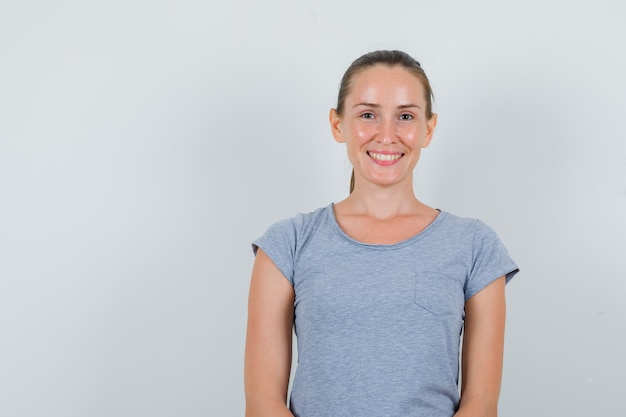 Mujer joven mirando y sonriendo en camiseta gris, vista frontal.