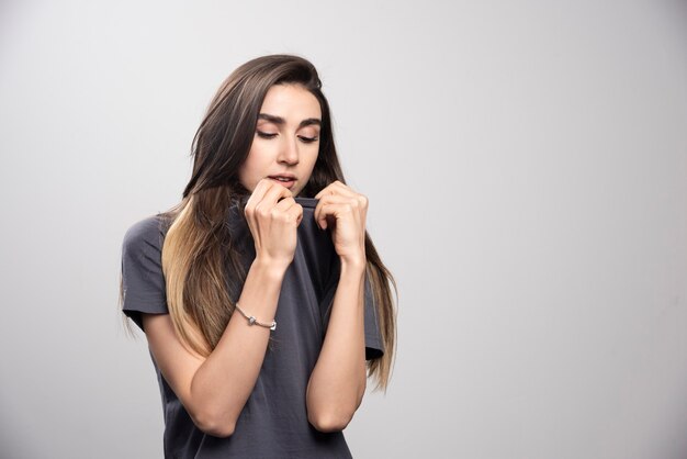 Mujer joven mirando su camiseta sobre un fondo gris.