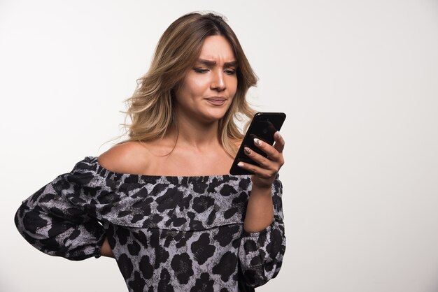 Mujer joven mirando su teléfono en la pared blanca.