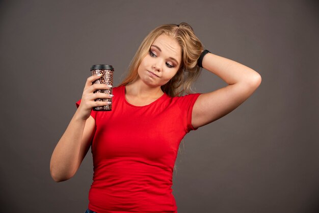 Mujer joven mirando una taza de café en la pared negra.