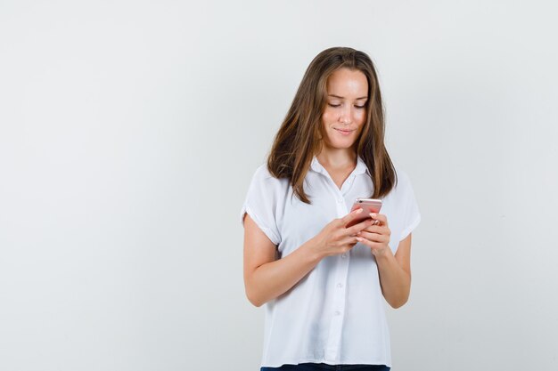 Mujer joven mirando el teléfono en blusa blanca y mirando concentrado