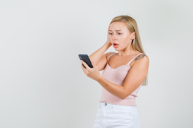 Mujer joven mirando el teléfono móvil en camiseta, minifalda y mirando arrepentido.