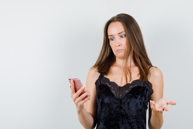 Mujer joven mirando el teléfono móvil en camiseta negra y mirando desconcertado