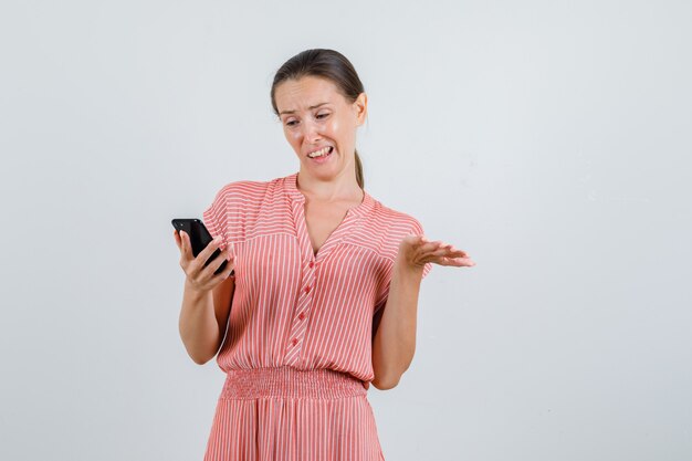 Mujer joven mirando el teléfono móvil con vestido de rayas y mirando irritado, vista frontal.