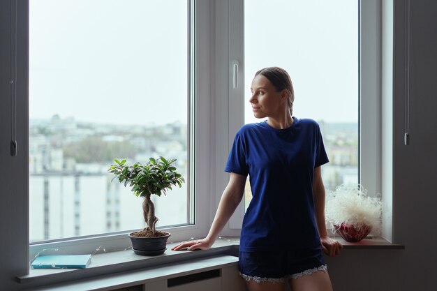 Mujer joven mirando por la ventana a la ciudad