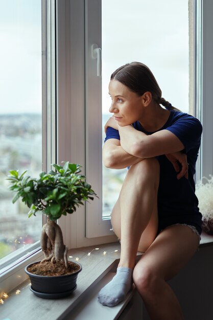 Mujer joven mirando por la ventana a la ciudad