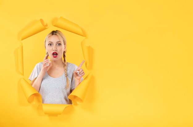 Mujer joven mirando desde la ventana facial de fondo de papel amarillo rasgado venta interior