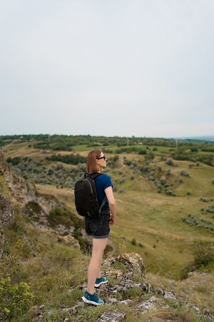 Mujer joven con mochila de pie en el borde del acantilado y mirando al cielo y la hermosa naturaleza.