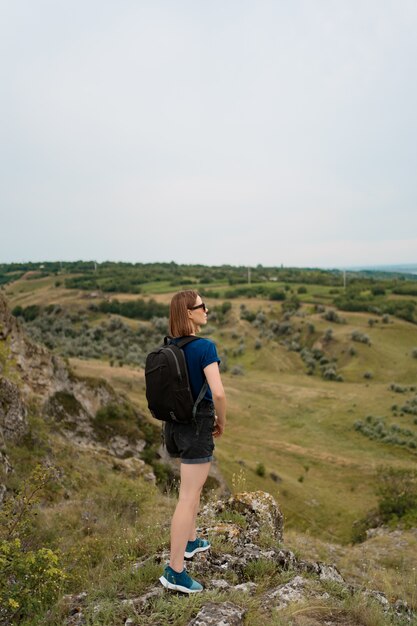 Mujer joven con mochila de pie en el borde del acantilado y mirando al cielo y la hermosa naturaleza.