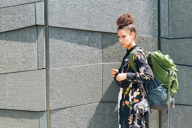 Mujer joven con mochila de pie junto a la pared al aire libre