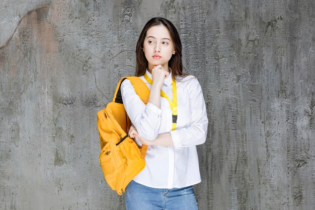 Mujer joven con mochila de pie sobre una pared gris. foto de alta calidad