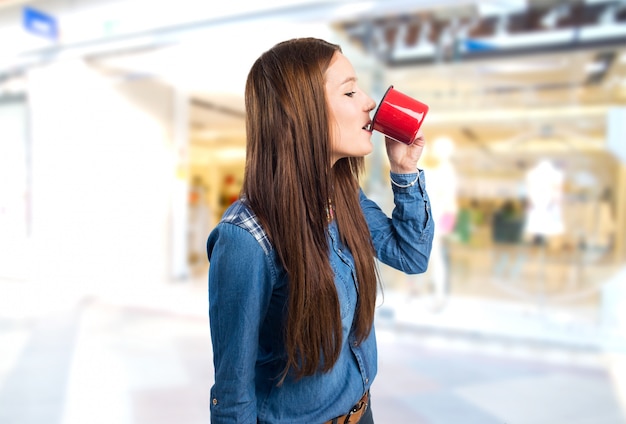 Mujer joven de moda que bebe de una taza roja