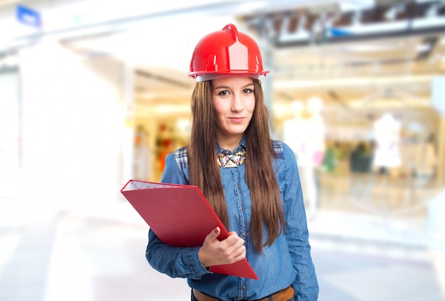 Mujer joven de moda que sostiene una carpeta de color rojo y que lleva un casco