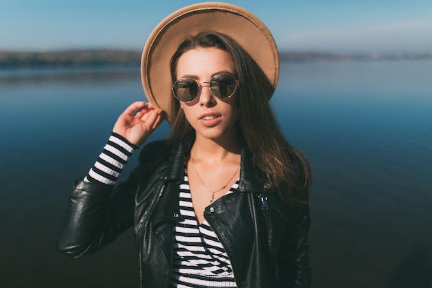 Mujer joven modelo chica posando en día de otoño en la orilla del lago vestida con ropa casual