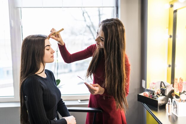 Mujer joven modelo en salón de belleza está haciendo maquillaje de noche